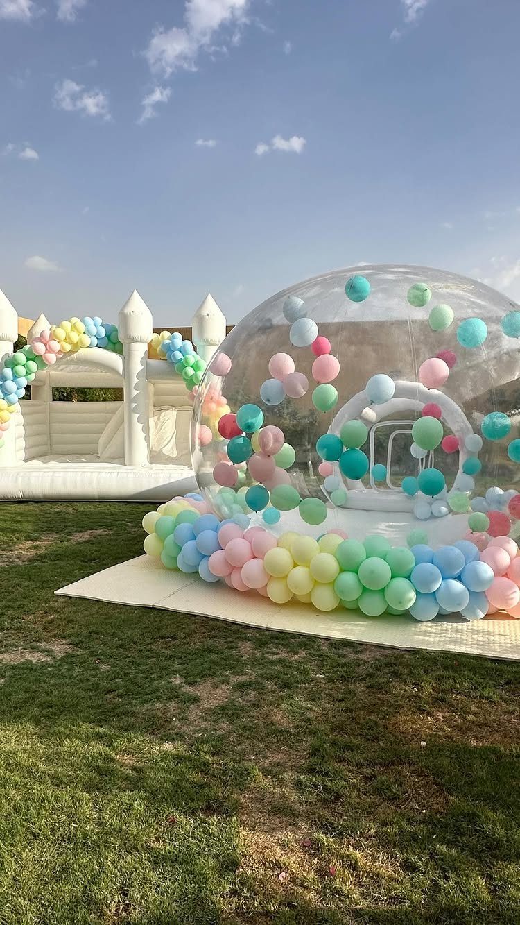 Clear inflatable dome filled with pastel balloons next to a white bouncy castle.