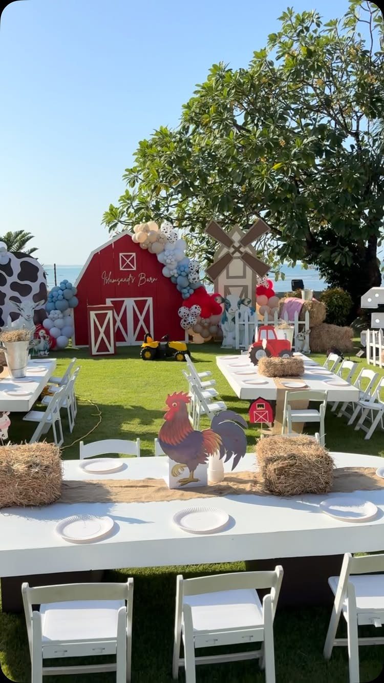 Farm themed party setup with red barn backdrop, white tables, and hay bales.