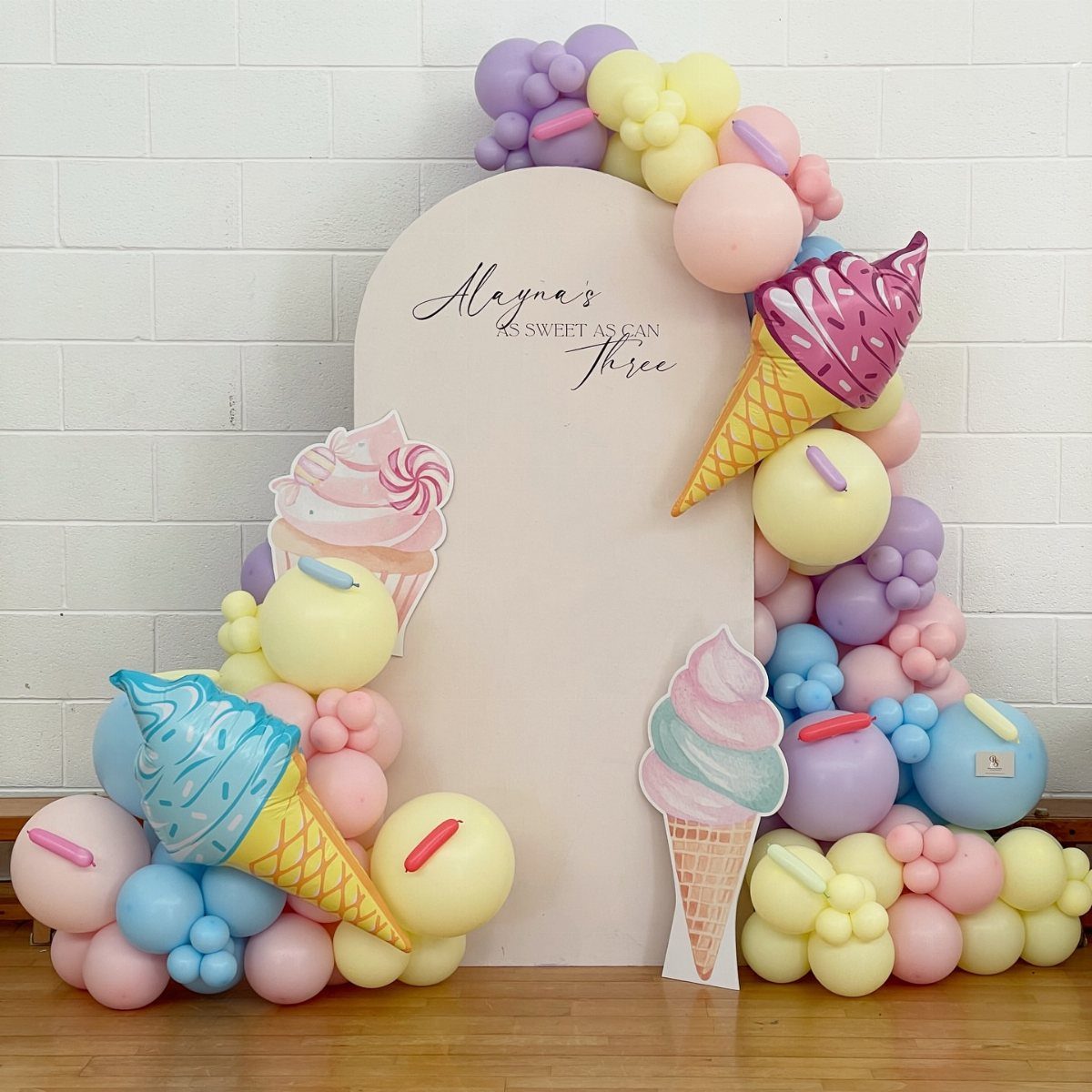 Pastel balloon arch with ice cream cone cutouts surrounding a pink birthday backdrop.