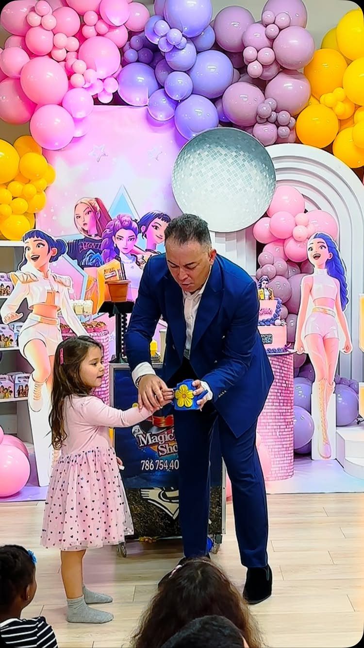 Magician in blue suit performing a trick for a young girl at a party