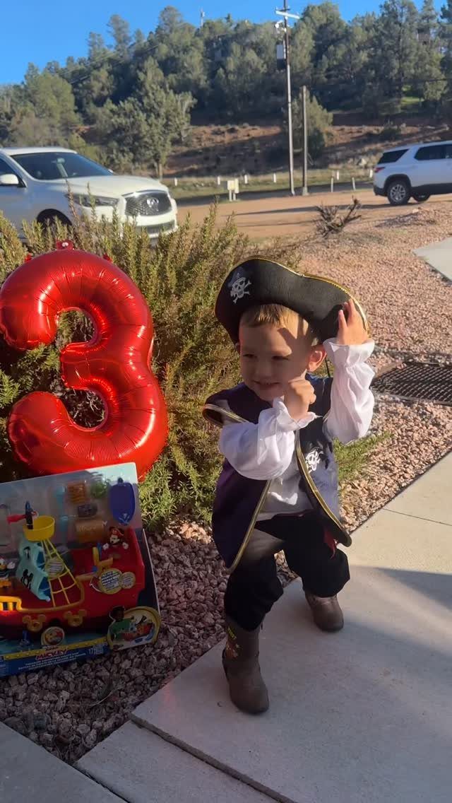 Child in pirate costume standing next to a large red number 3 balloon.