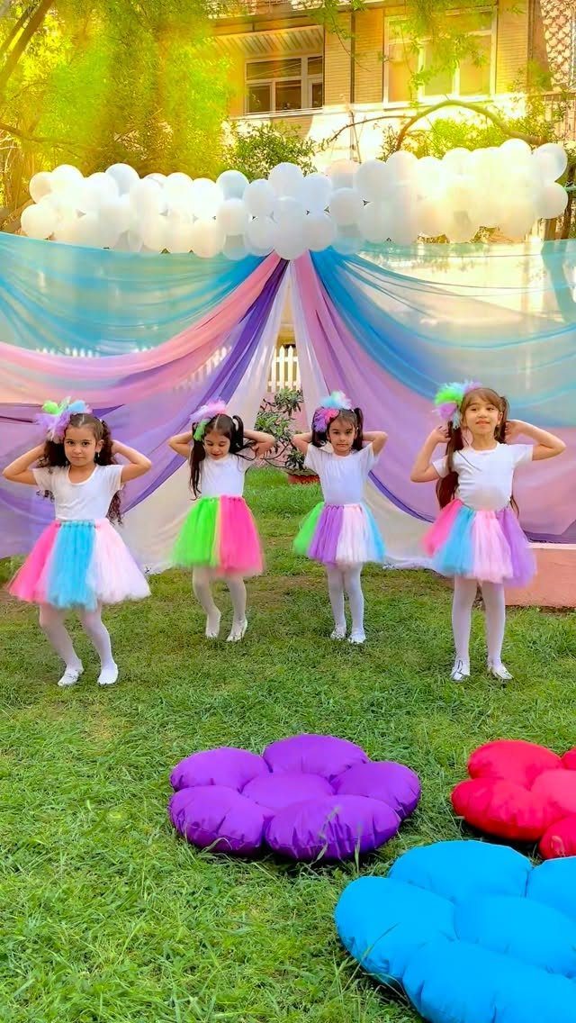 Four girls in rainbow tutus posing before a colorful backdrop and balloon arch.