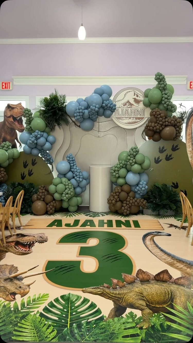 Dinosaur themed party decor with balloon arches, a large number 3, and dinosaurs.