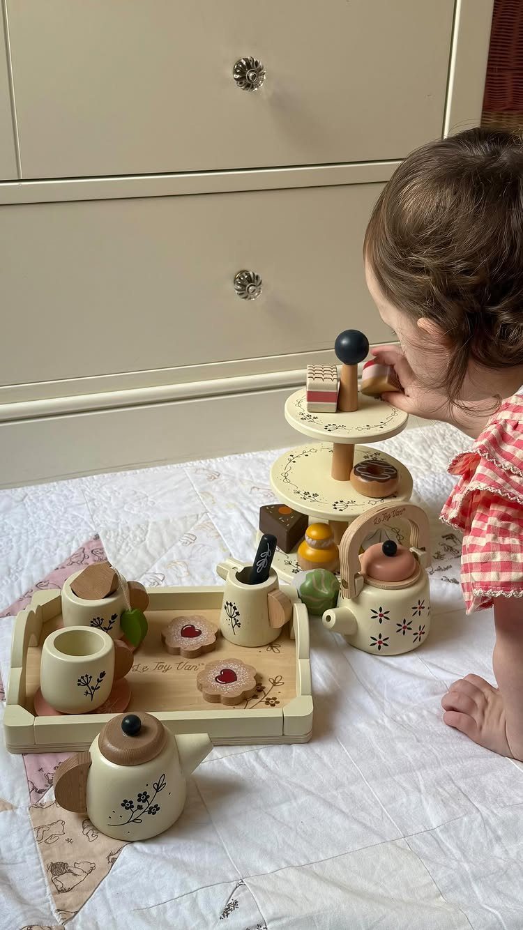 Young child playing with a wooden tea set on a white fabric surface.