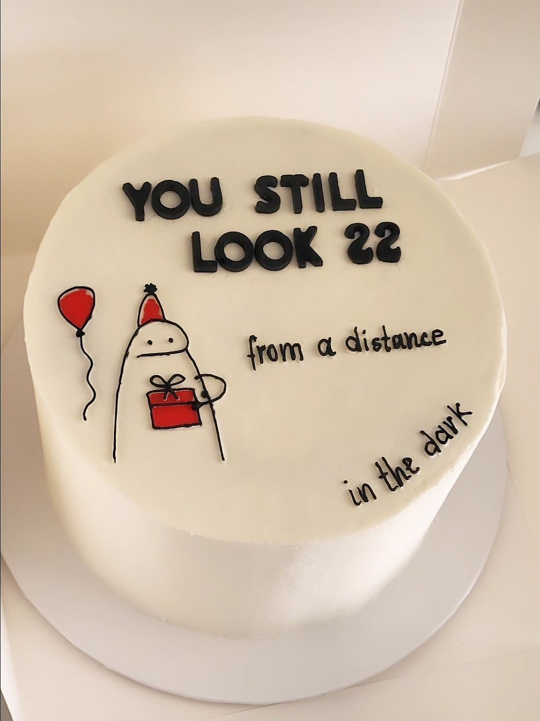White round birthday cake with humorous text about aging and a simple drawing.