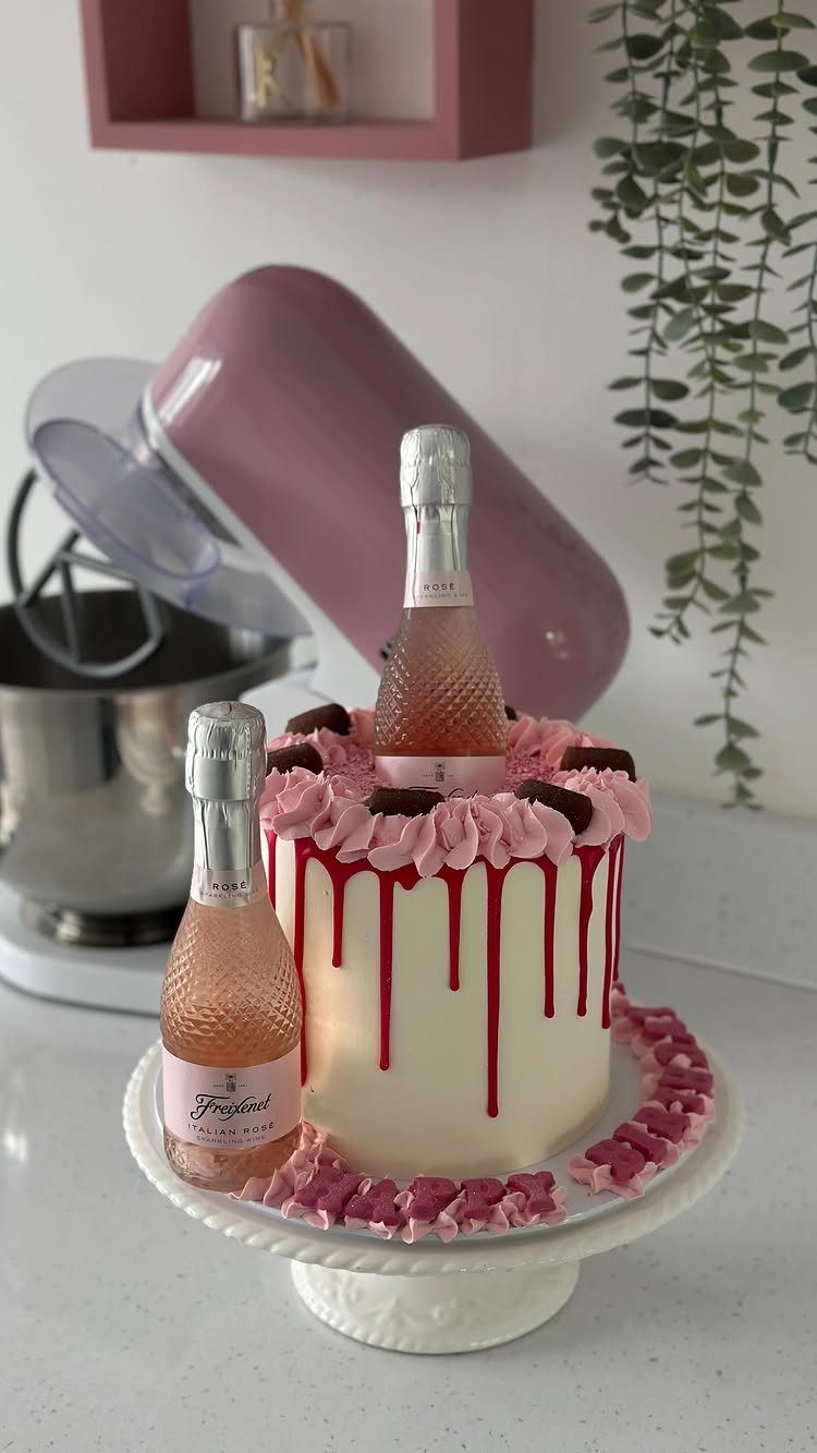 White cake with pink drips and a mini bottle of bubbly on top.