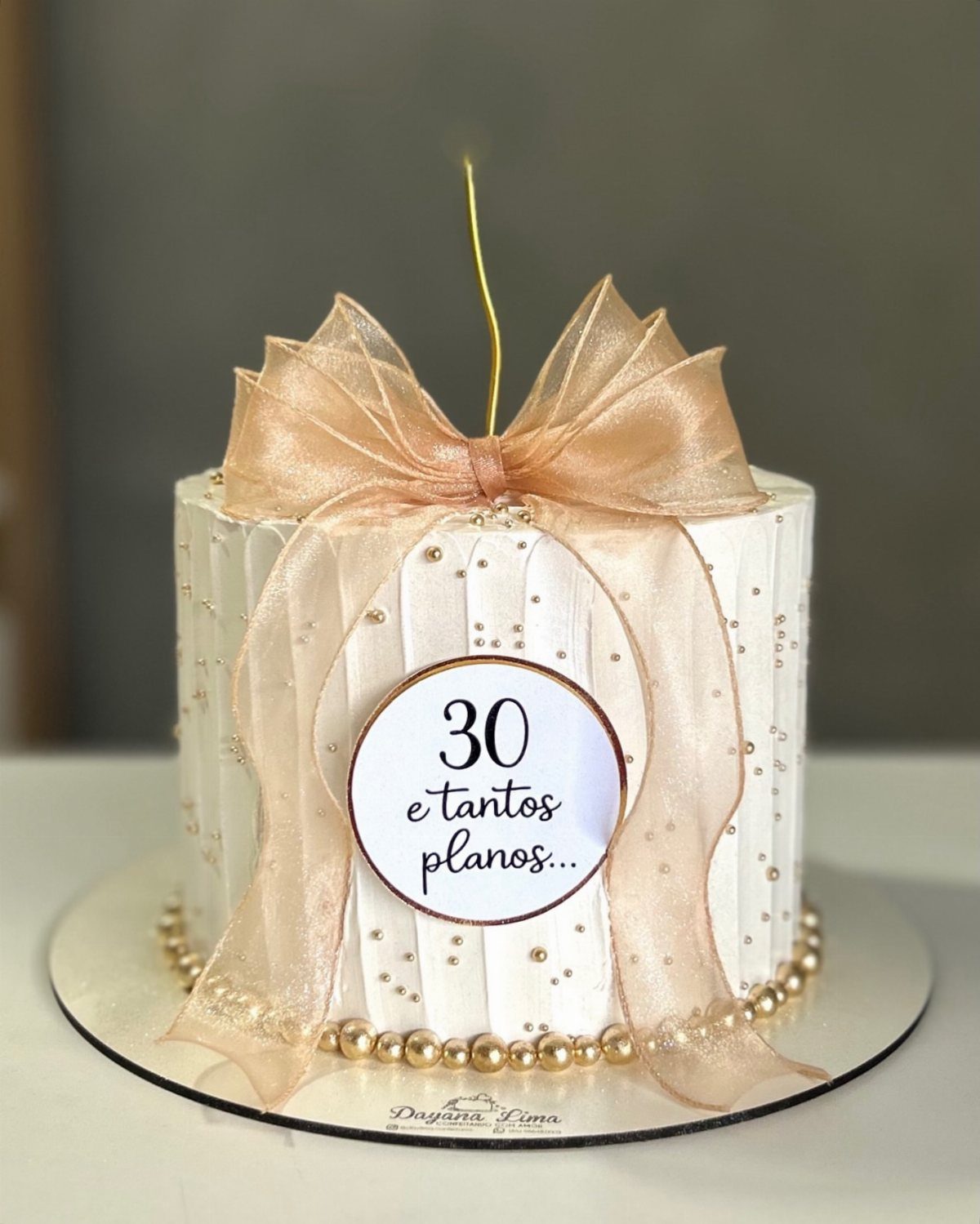Single tier white birthday cake with gold bow and 30th birthday plaque.