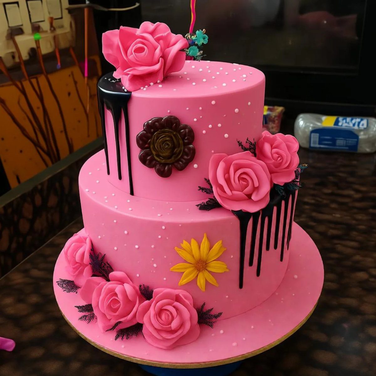 Two-tier pink birthday cake with sugar roses and black chocolate drip decoration.