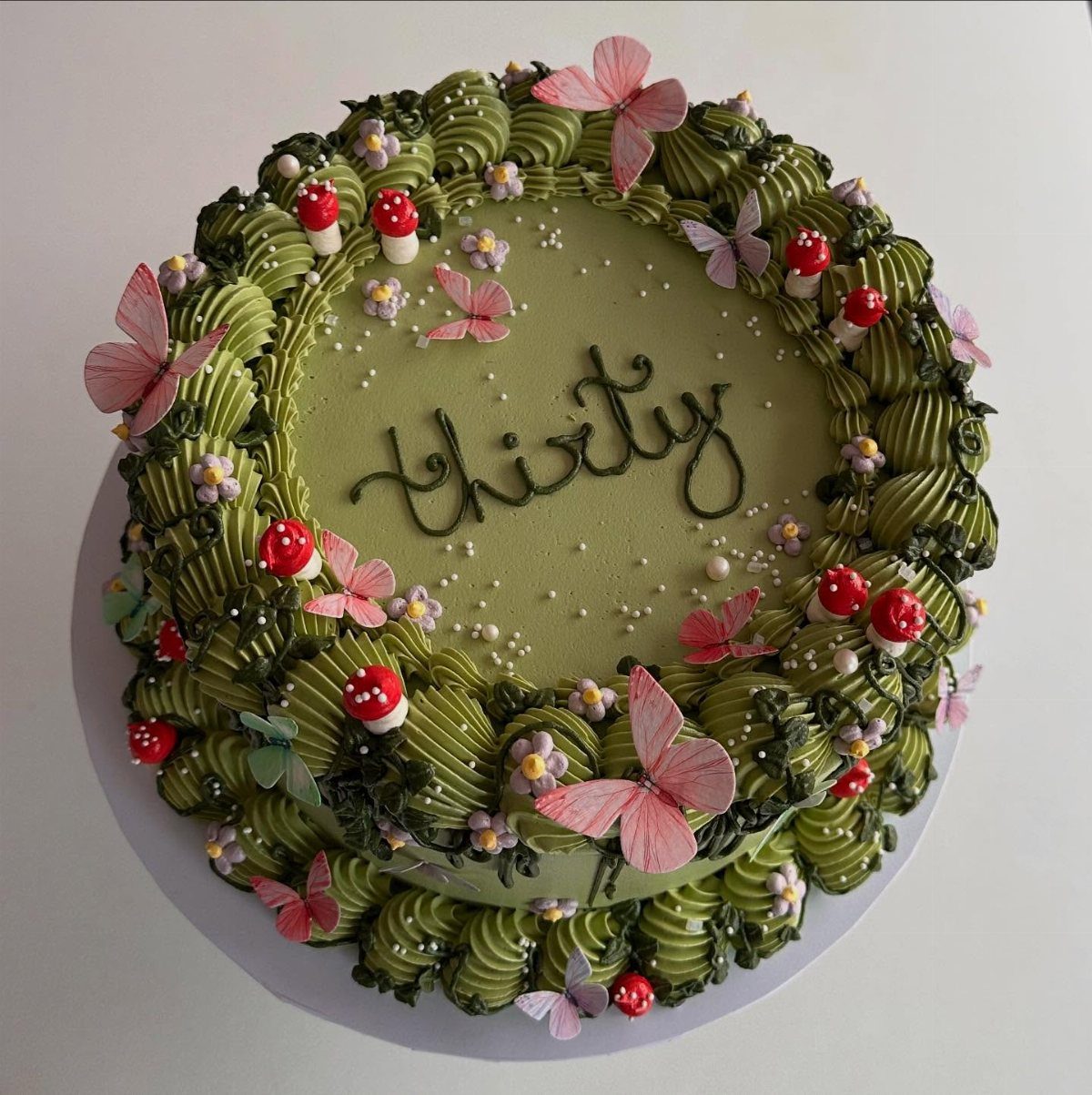 Green birthday cake with mushrooms, pink butterflies, and the word thirty written on top.