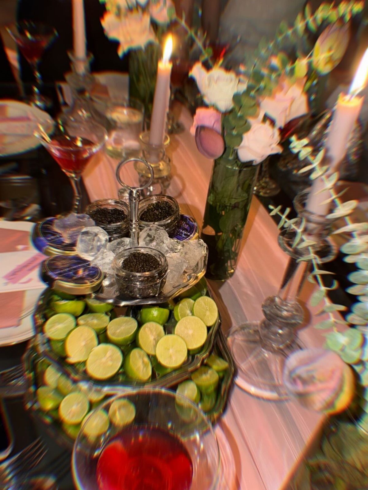 Tiered platter of limes and cocktails on a decorated table with candles and flowers.