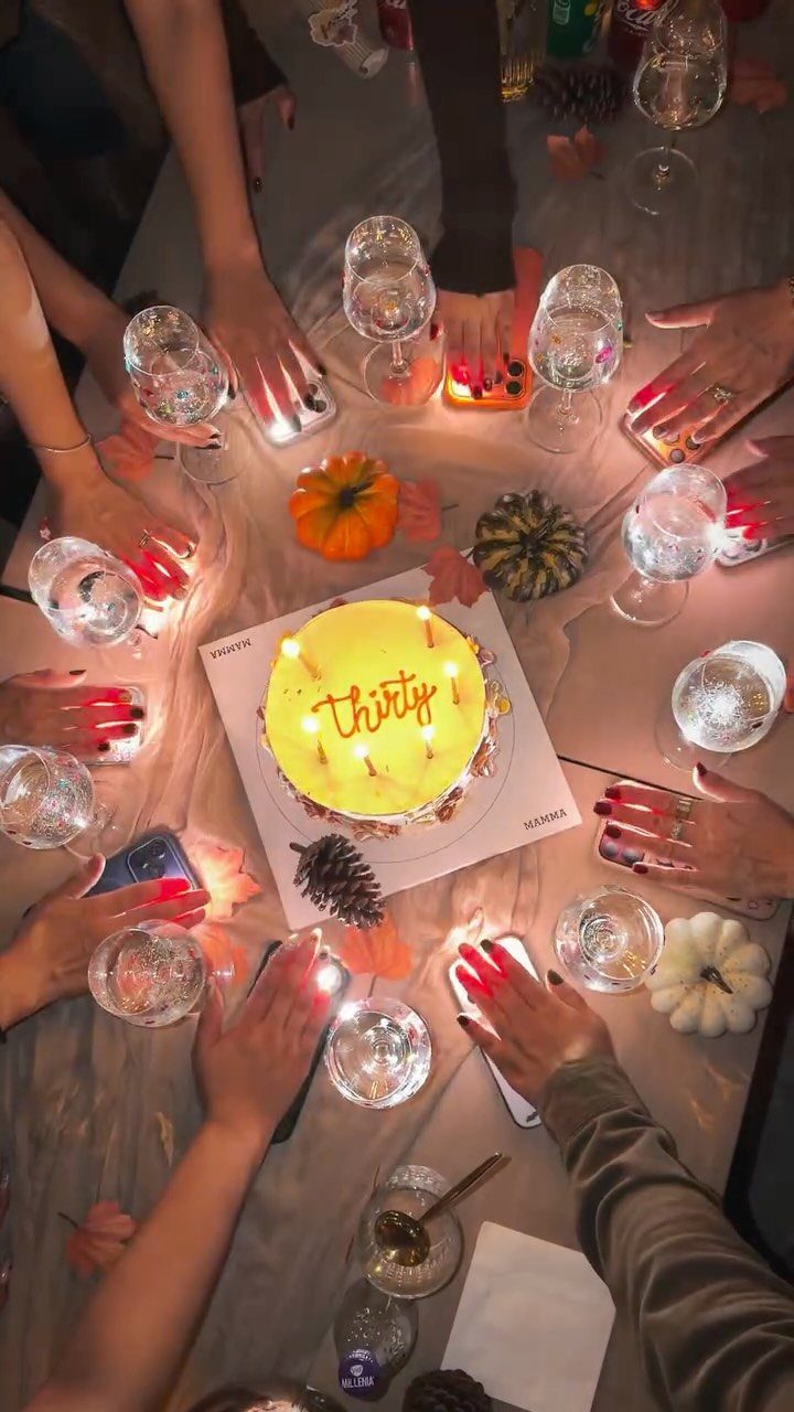 Yellow birthday cake with thirty written on it surrounded by guests' hands and wine glasses