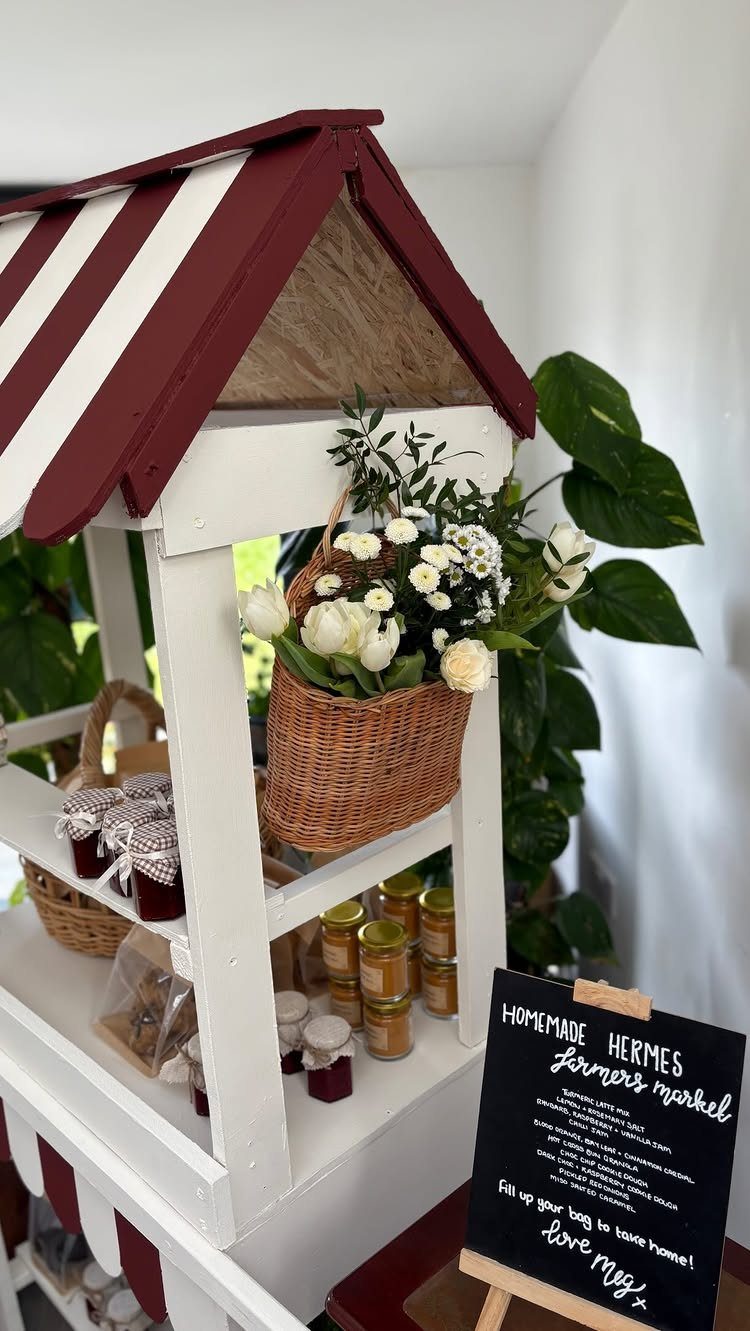 White wooden market stall with striped roof displaying jars and white flowers.