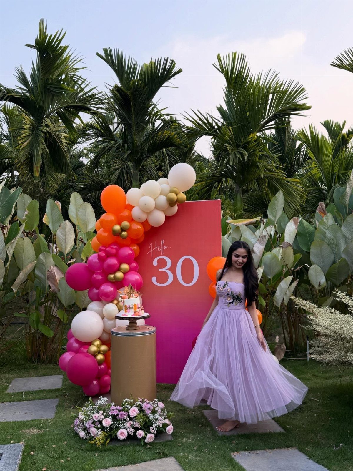 Woman in purple gown posing by 30th birthday decorations in a lush garden