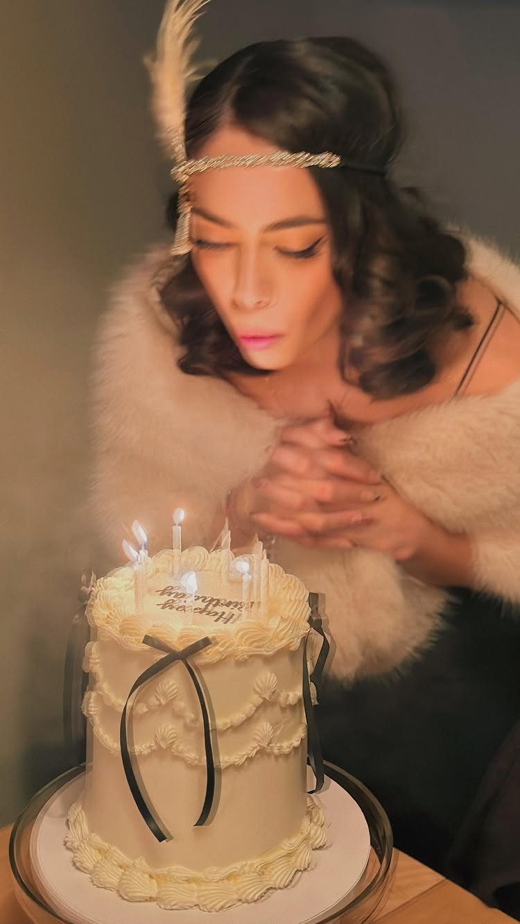Woman in 1920s flapper attire with a feather headband blowing out birthday candles.