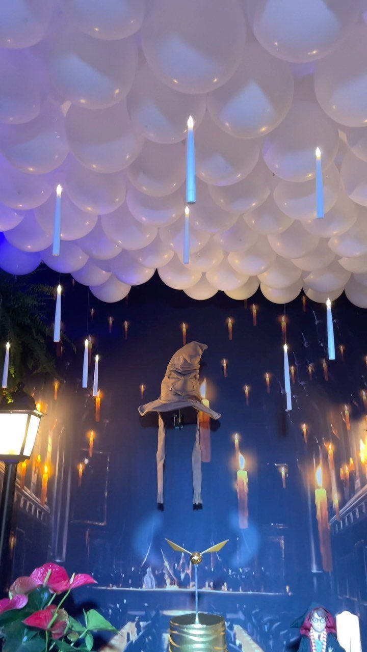 Harry Potter themed party decorations with floating candles, white balloons, and a wizard hat.