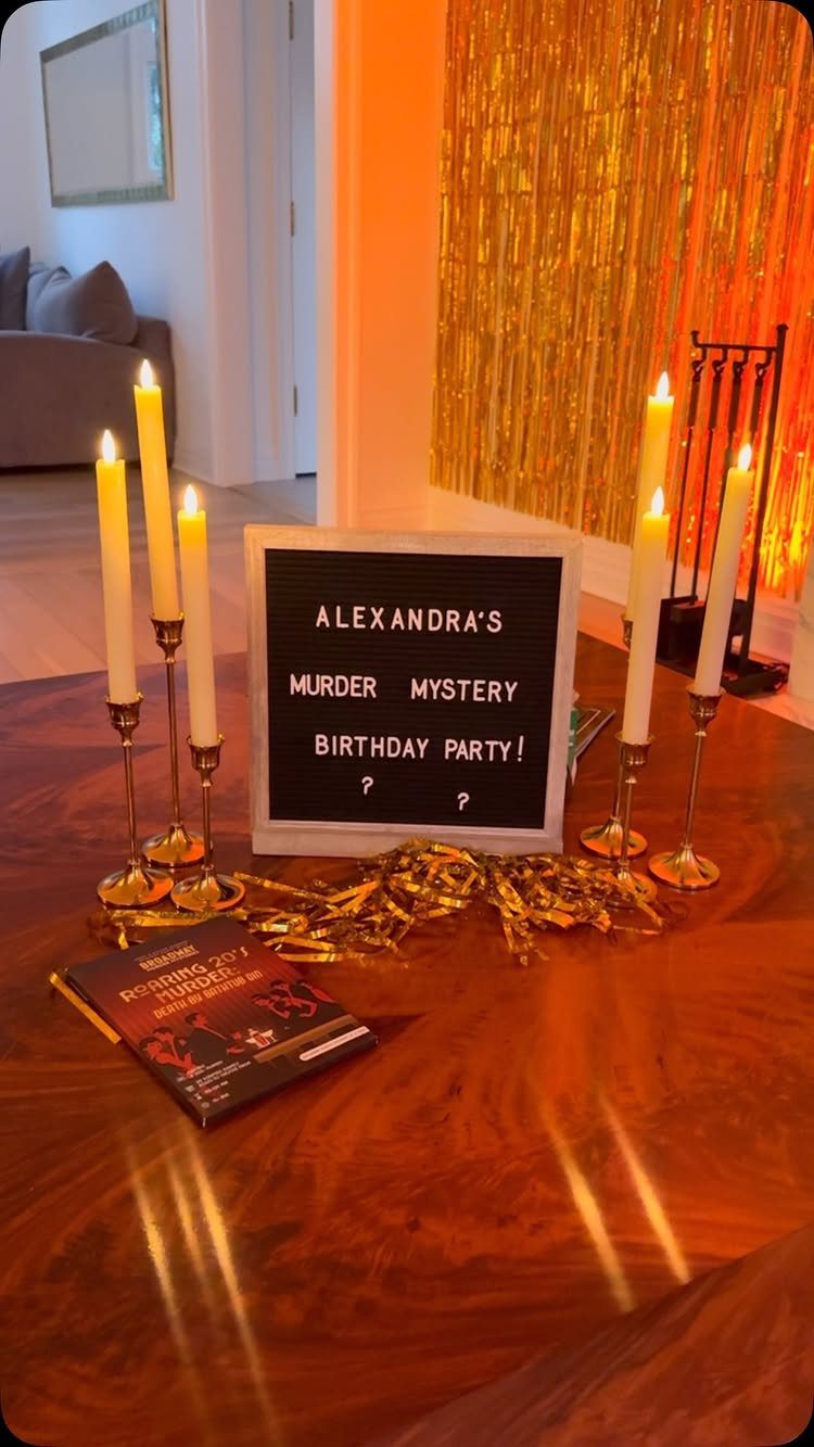 Birthday party setup with a murder mystery sign, gold candles, and tinsel backdrop.