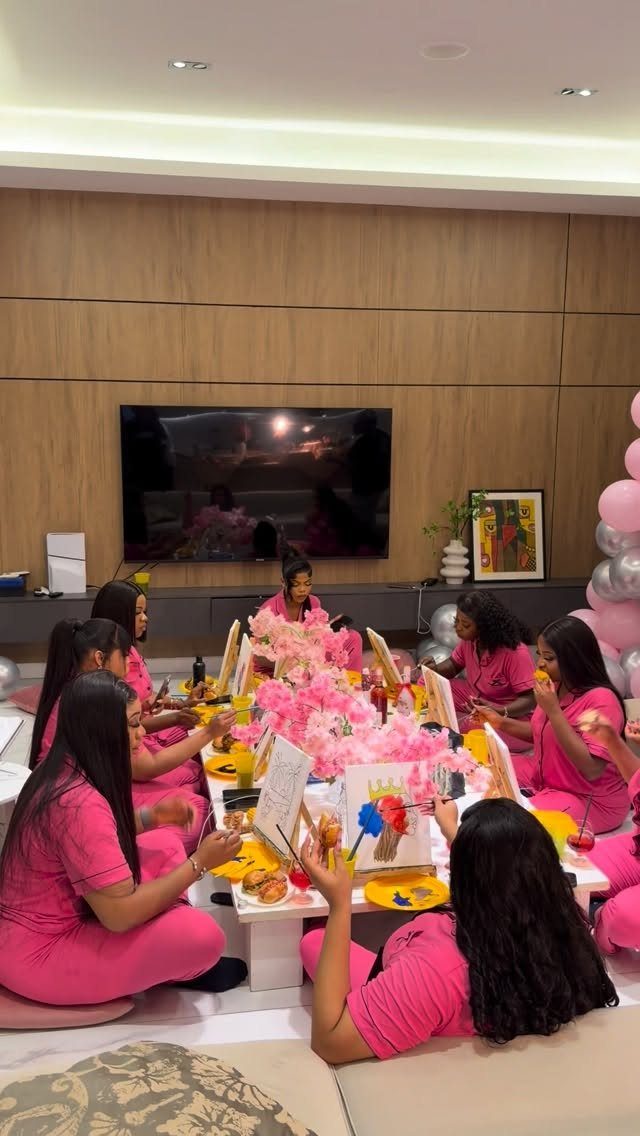 Women in pink pajamas painting on canvases at a decorated party table.