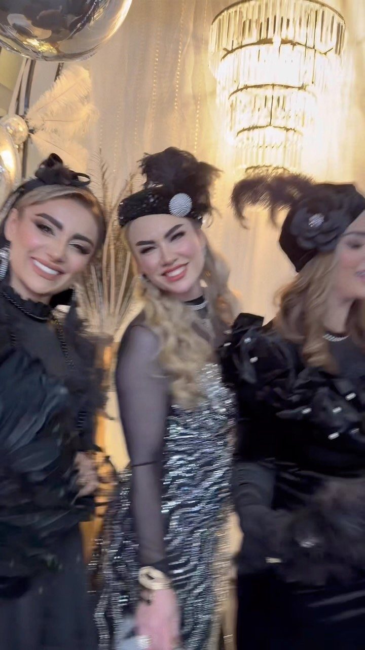 Three women in 1920s flapper dresses and headbands posing under a chandelier.