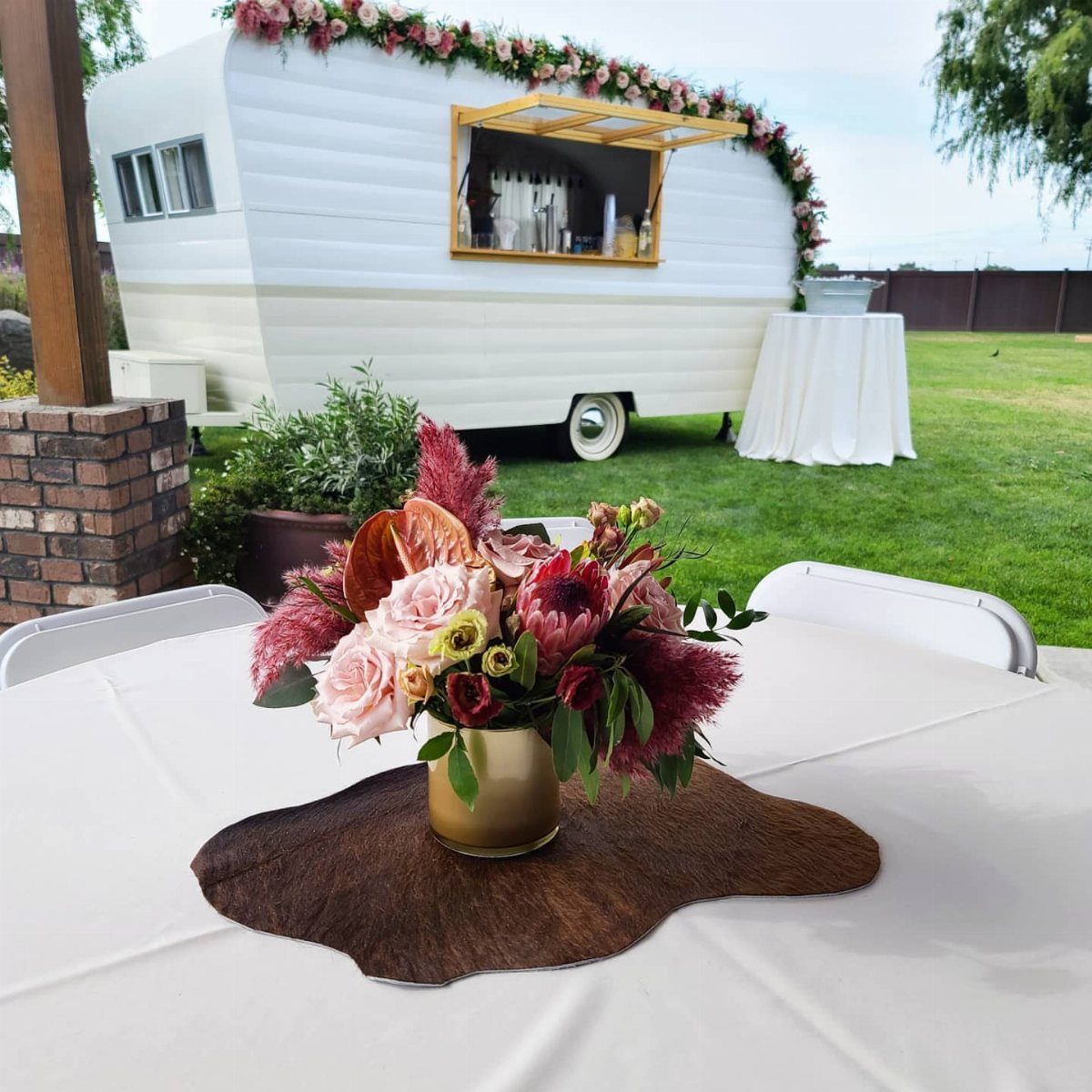 White vintage trailer bar with floral decorations on a green lawn with table settings