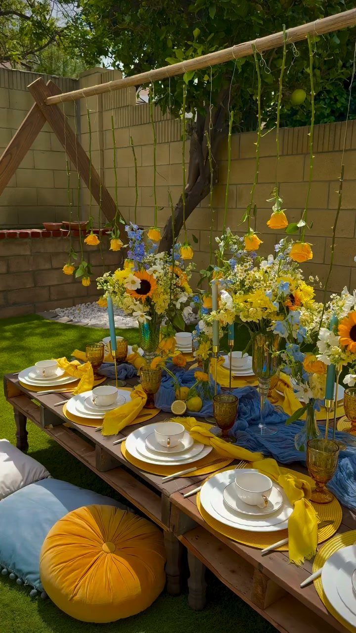Low wooden picnic table with yellow and blue decor and floor cushions outdoors