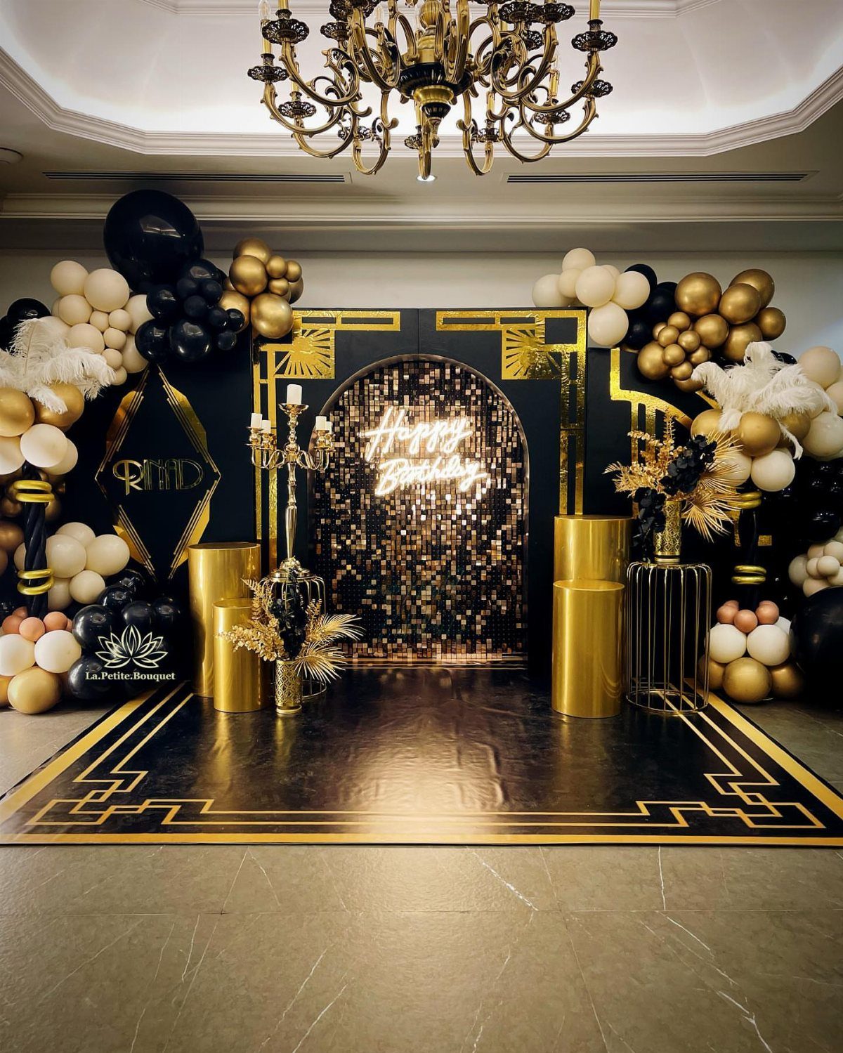 Black and gold Art Deco birthday party setup with balloons and neon sign.