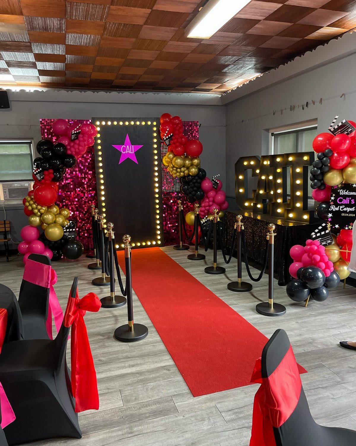 Red carpet entrance with marquee lights, black and red balloons, and stanchions.