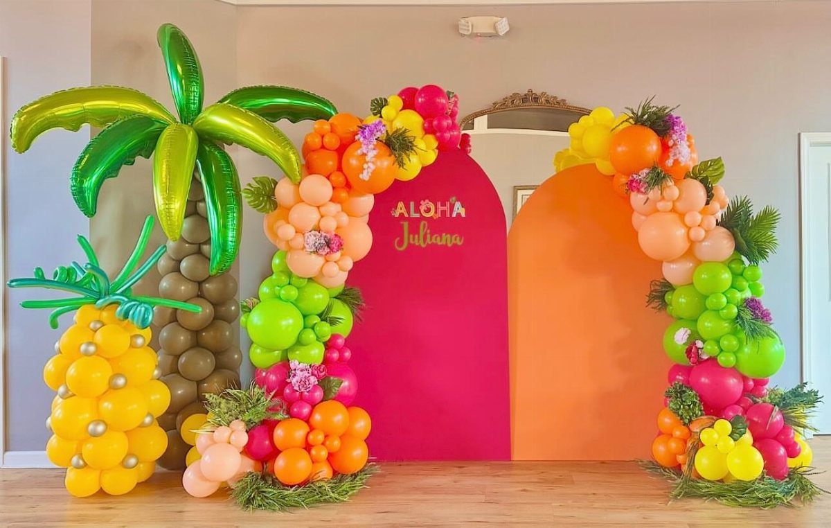 Tropical party decorations with palm tree and pineapple balloons and colorful arched backdrops.