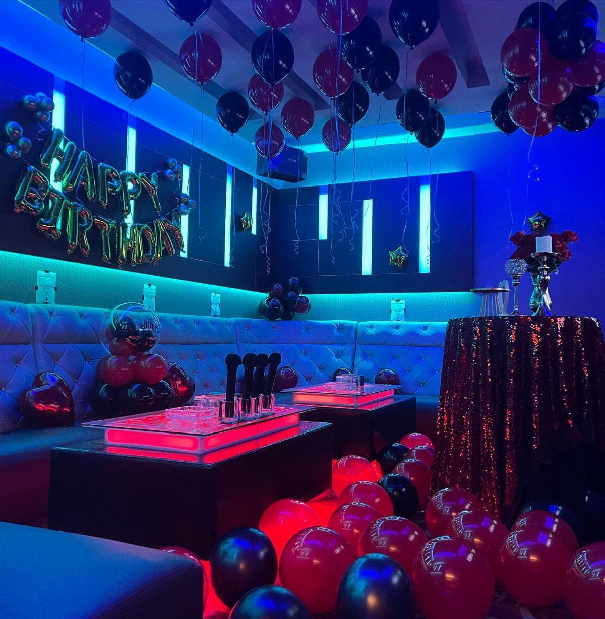 Party room with blue neon lights, red and black balloons, and birthday banner.