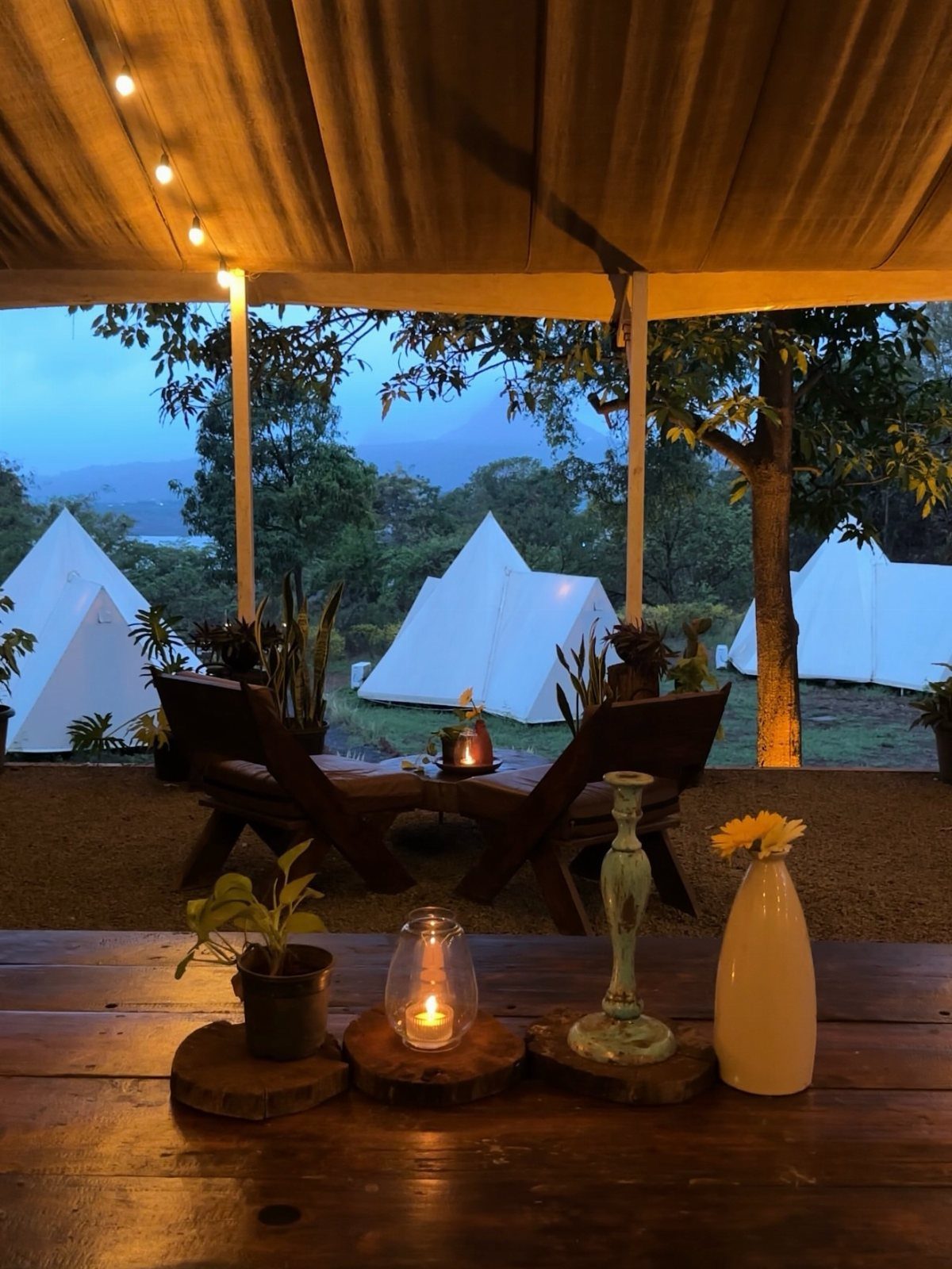 Wooden table with candle and vase overlooking white glamping tents in a mountain valley