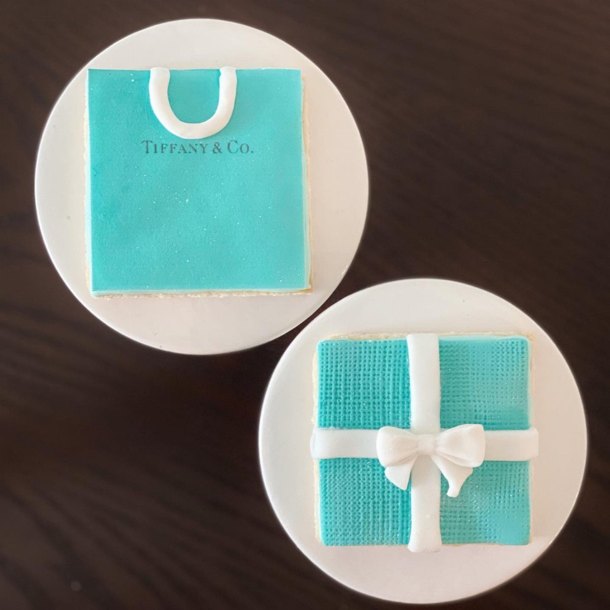 Turquoise Tiffany and Co. themed cookies on white cupcakes on a dark surface