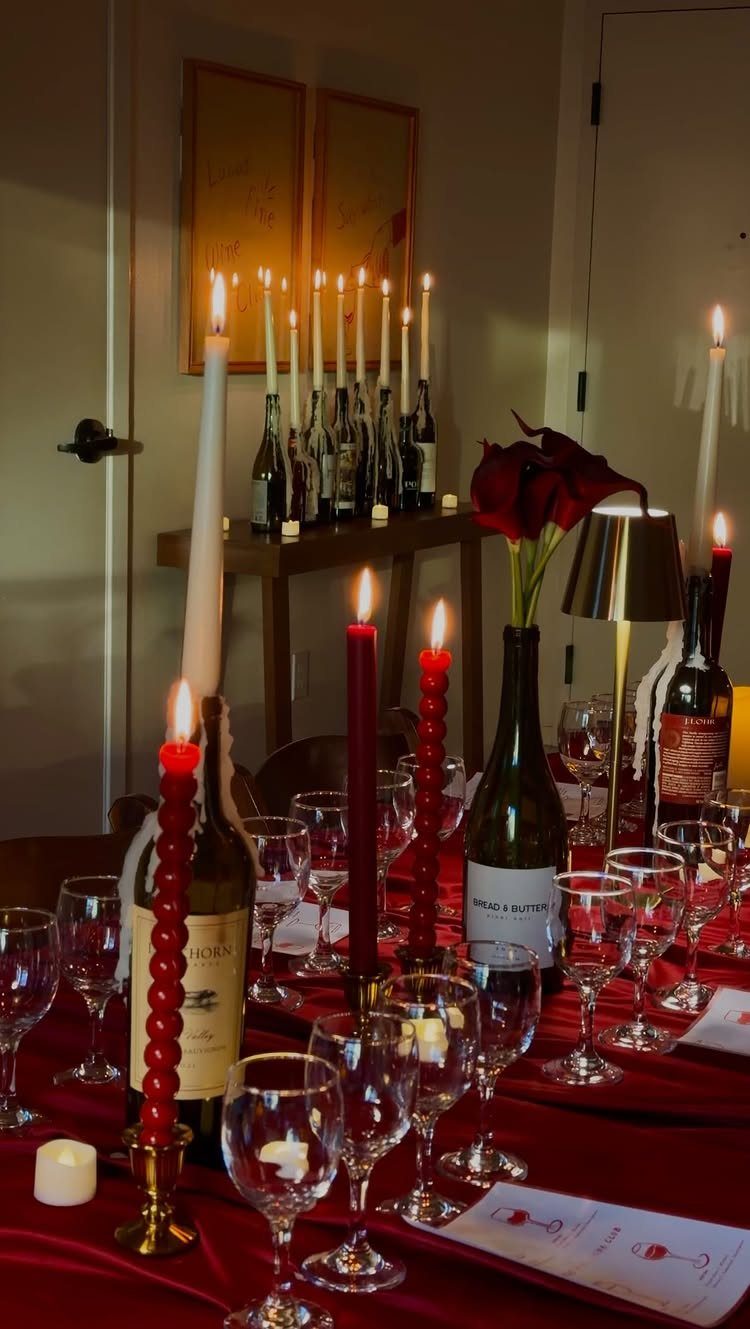 Wine tasting table with red tablecloth, lit candles, wine glasses, and wine bottles.