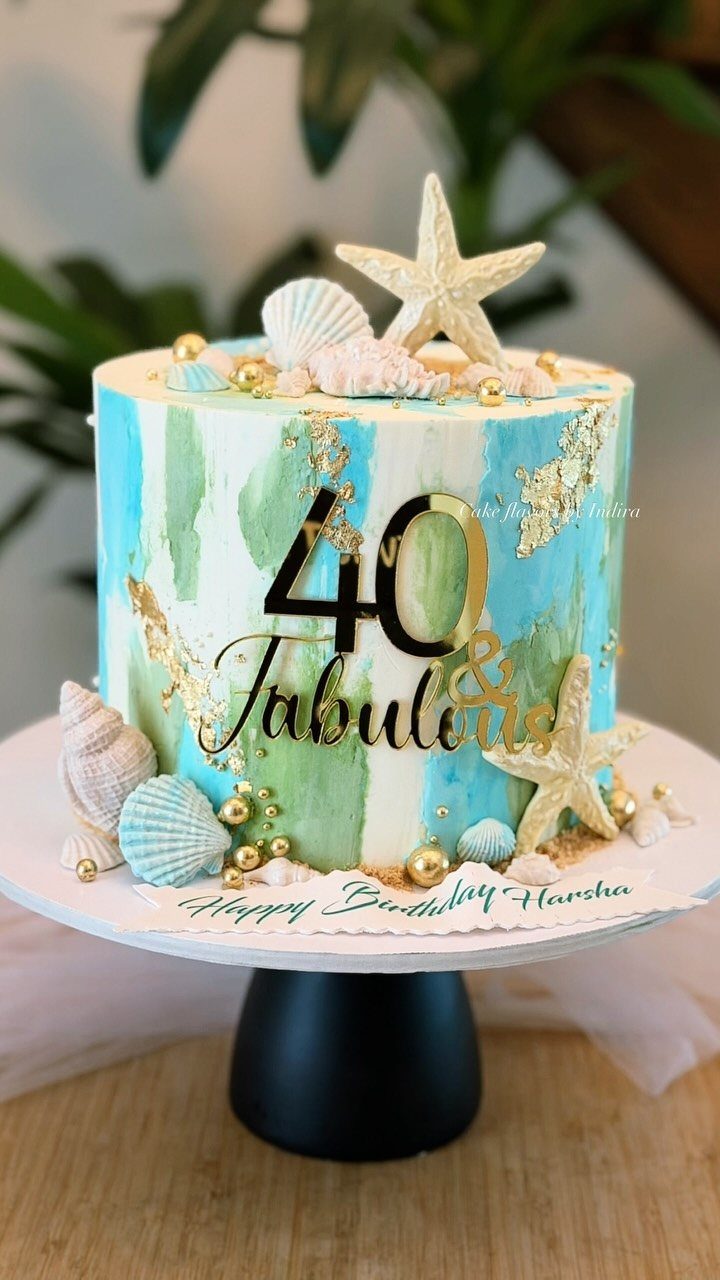 Beach themed 40th birthday cake with blue frosting, seashells, and gold topper.