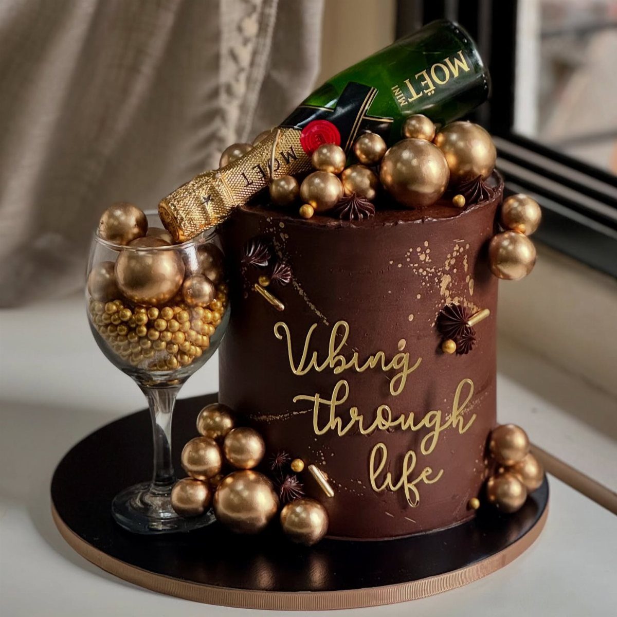 Chocolate cake decorated with gold spheres and a Moët champagne bottle on top.