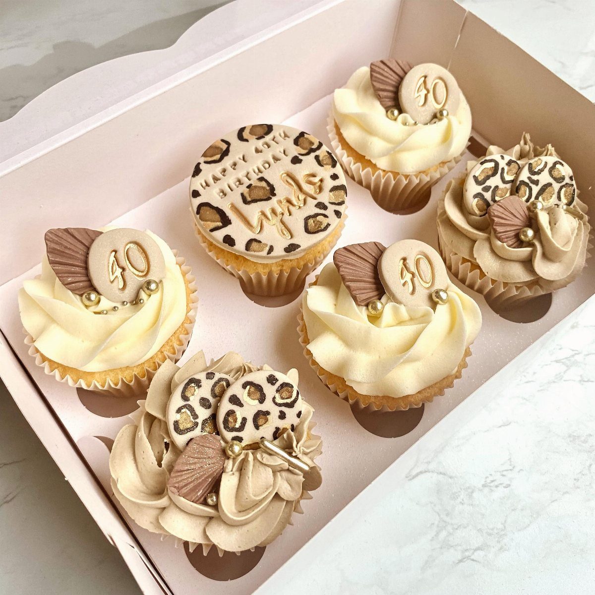 Six leopard print and gold themed cupcakes with 40th birthday toppers in a box