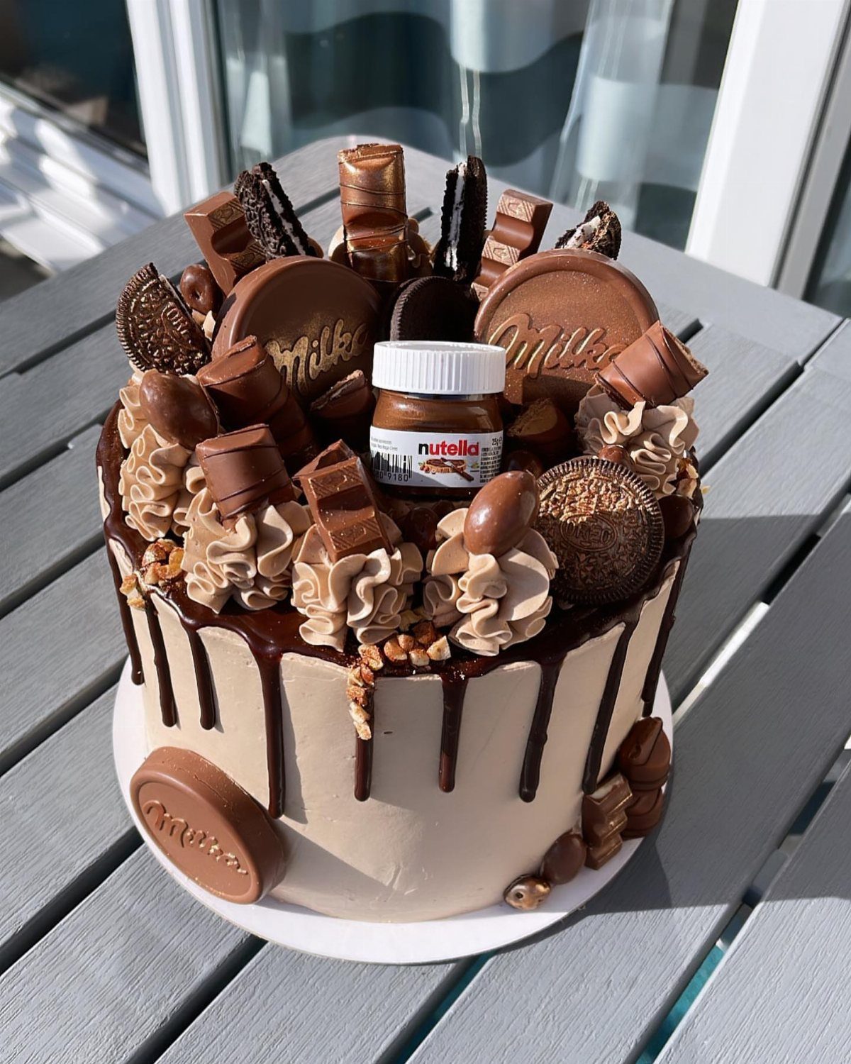 Chocolate cake topped with Nutella, Milka chocolates, and Ferrero Rocher on a table