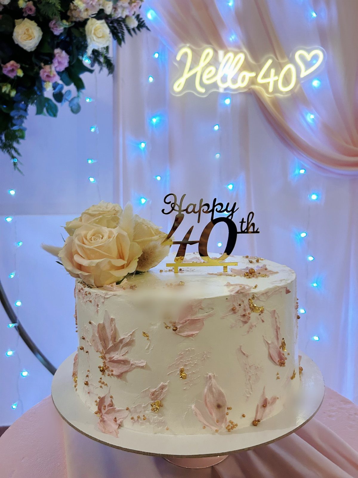 White single-tier birthday cake with pink accents, gold flakes, and Happy 40th topper.