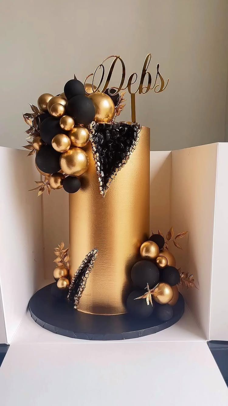Gold cylindrical cake with black and gold spheres and a gold name topper.