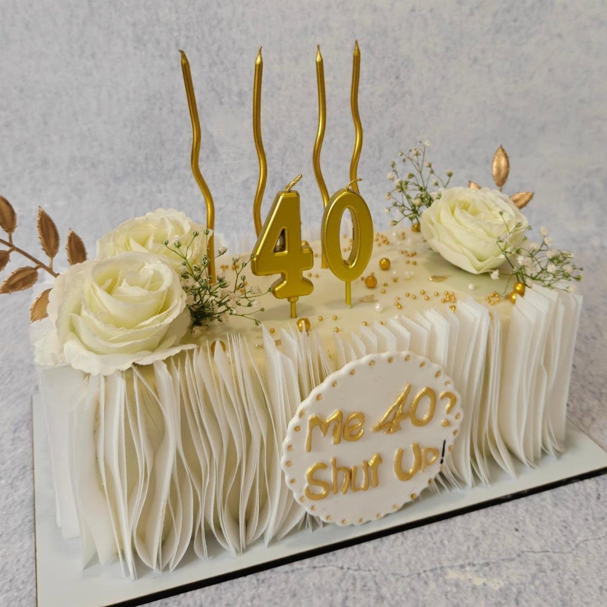 White rectangular 40th birthday cake with pleated frosting, white roses, and gold candles.
