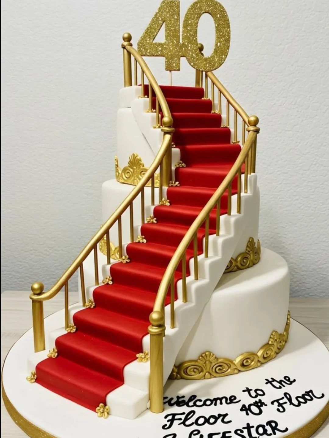 Three-tier white cake with red carpet stairs and gold 40 topper