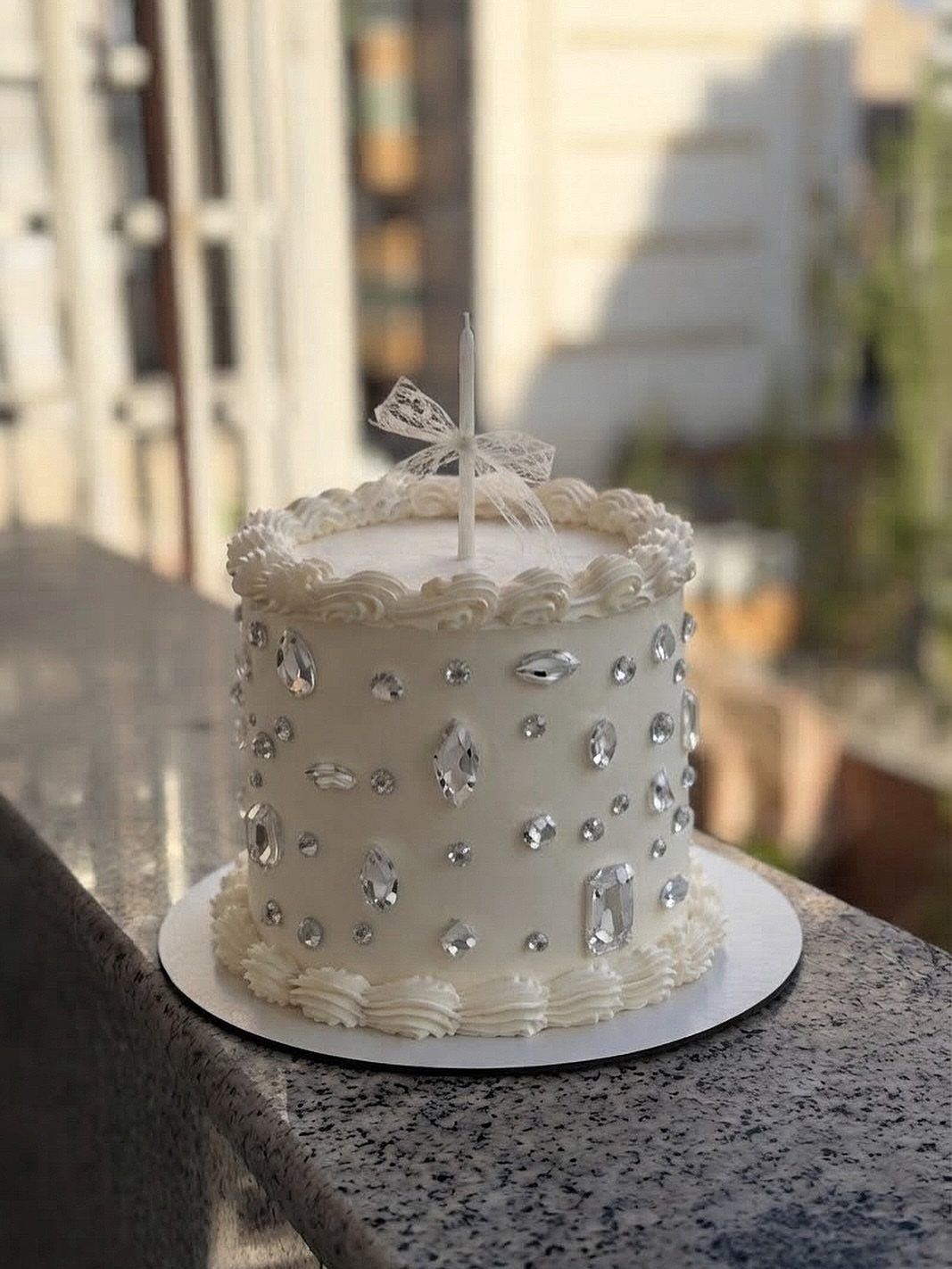 White frosted cake decorated with silver edible crystals and a single white candle.