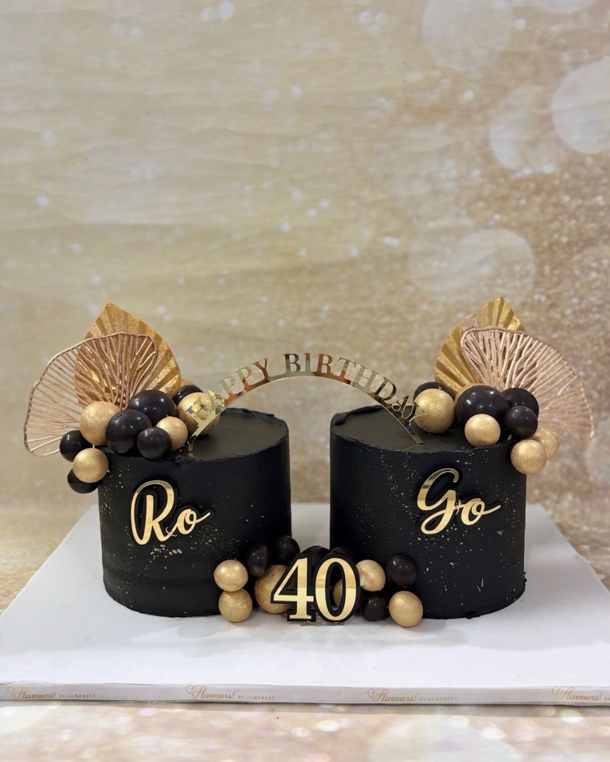 Two black frosted birthday cakes with gold accents, spheres, and a gold 40 topper.