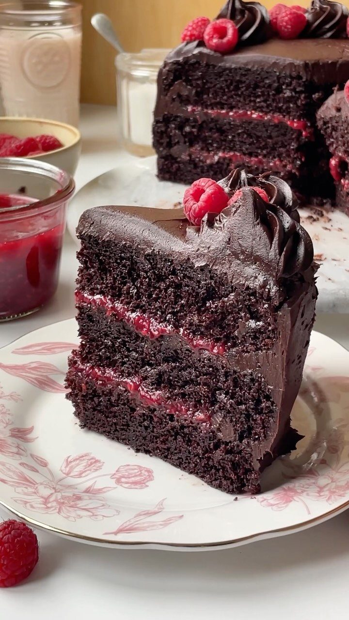 Chocolate layer cake slice with raspberry filling and frosting on a floral plate.