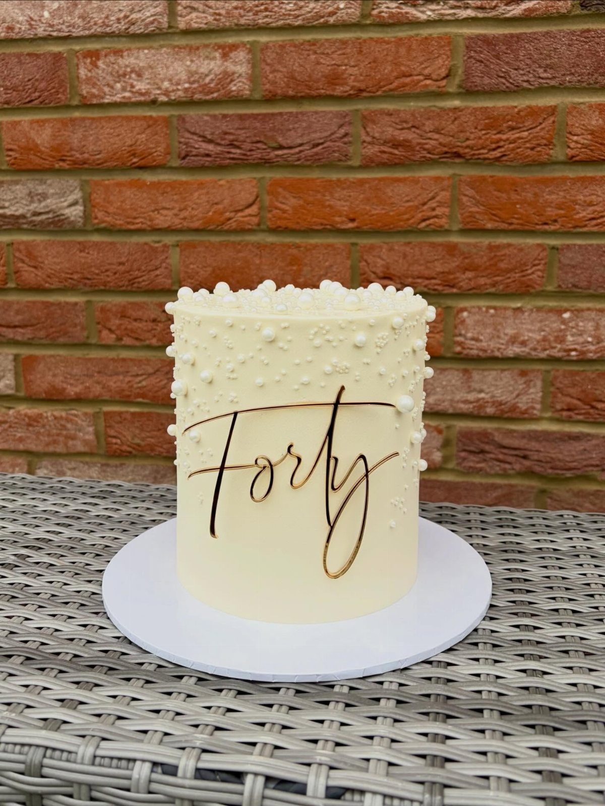 White frosted cake with gold Forty script and pearl decorations against brick wall