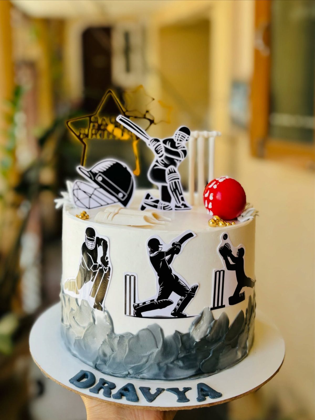 Cricket themed cake with player silhouettes, a red ball, and name Dravya.