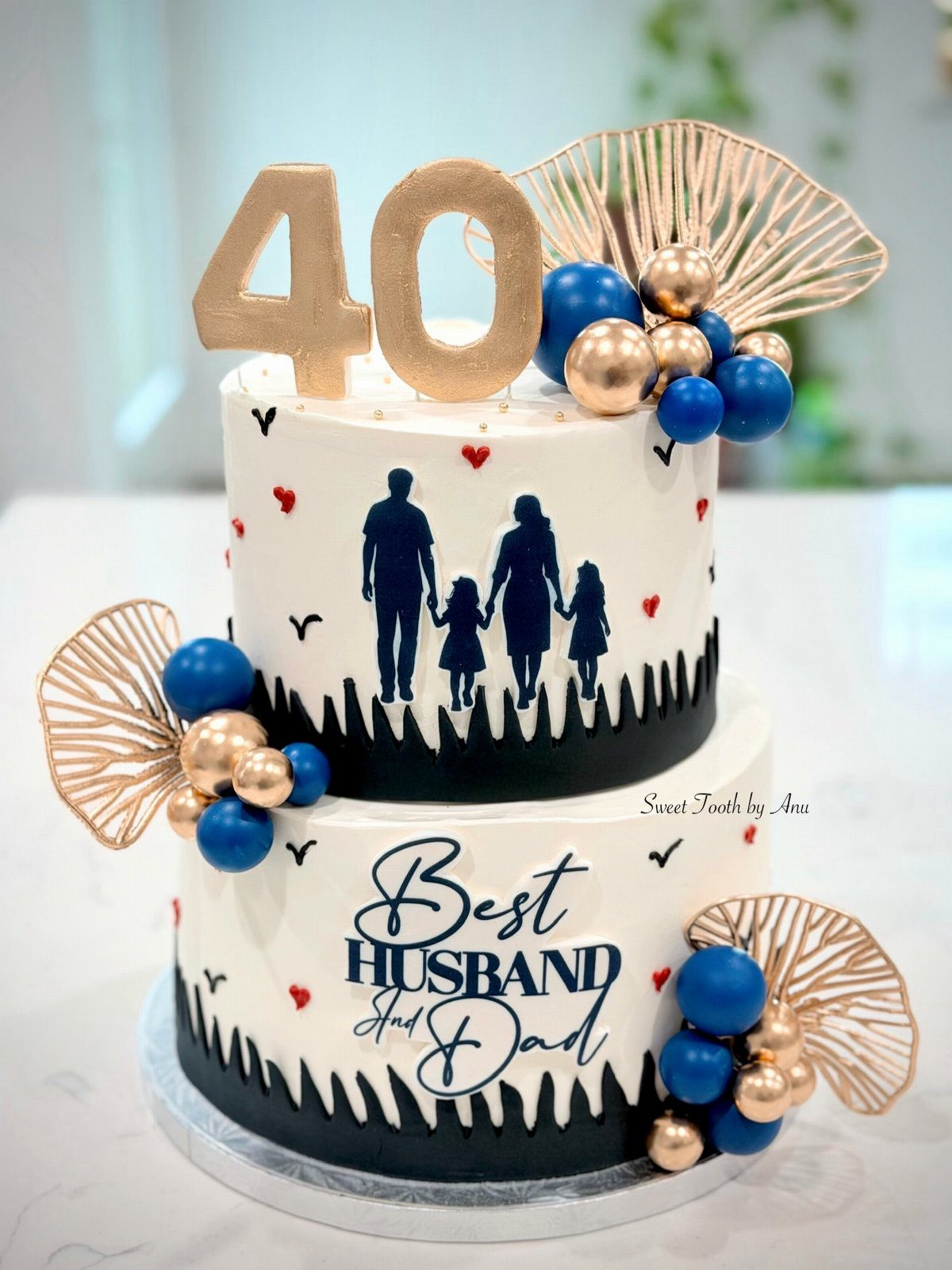 Two-tier white birthday cake with family silhouettes, gold 40 topper, and blue decorations.