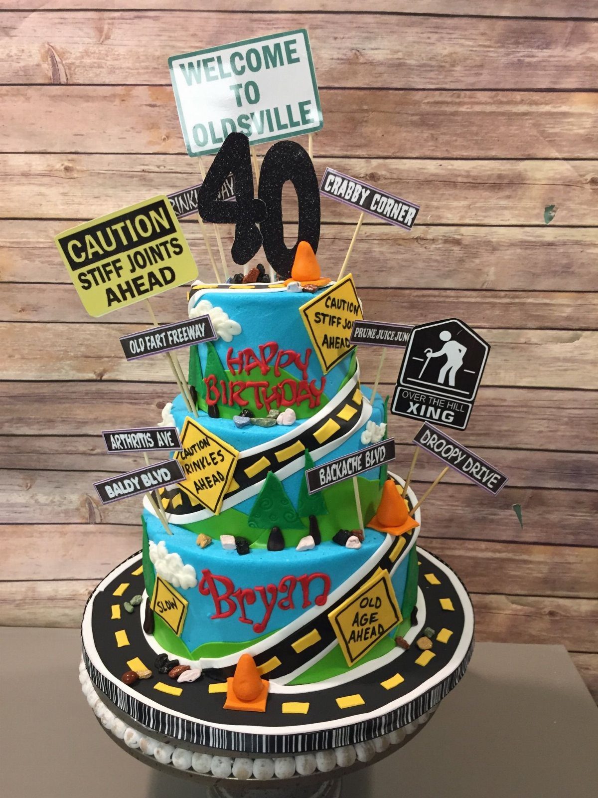 Three-tier blue birthday cake with humorous road signs and a black 40 topper.