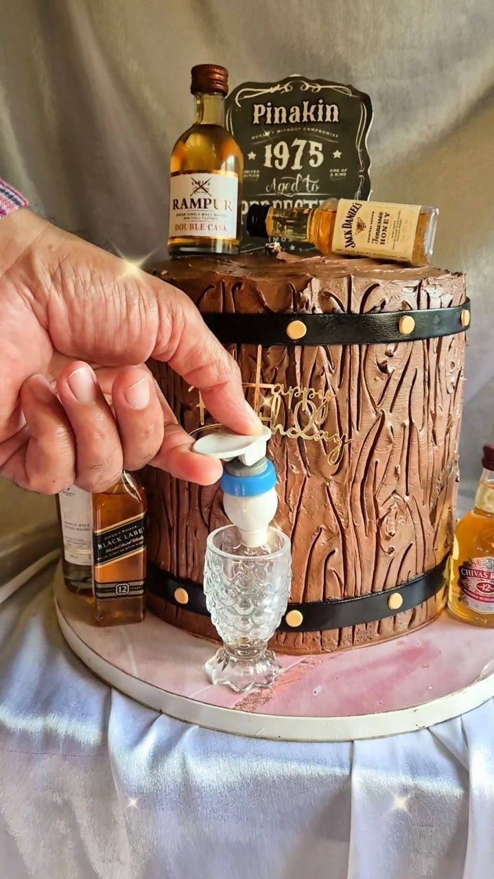 Whiskey barrel cake decorated with miniature bottles and a sign, being poured into glass.
