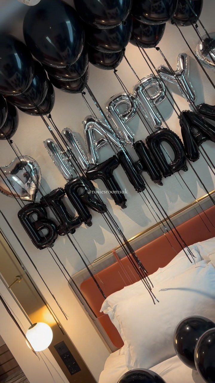 Silver and black birthday balloons floating over a bed with an orange headboard