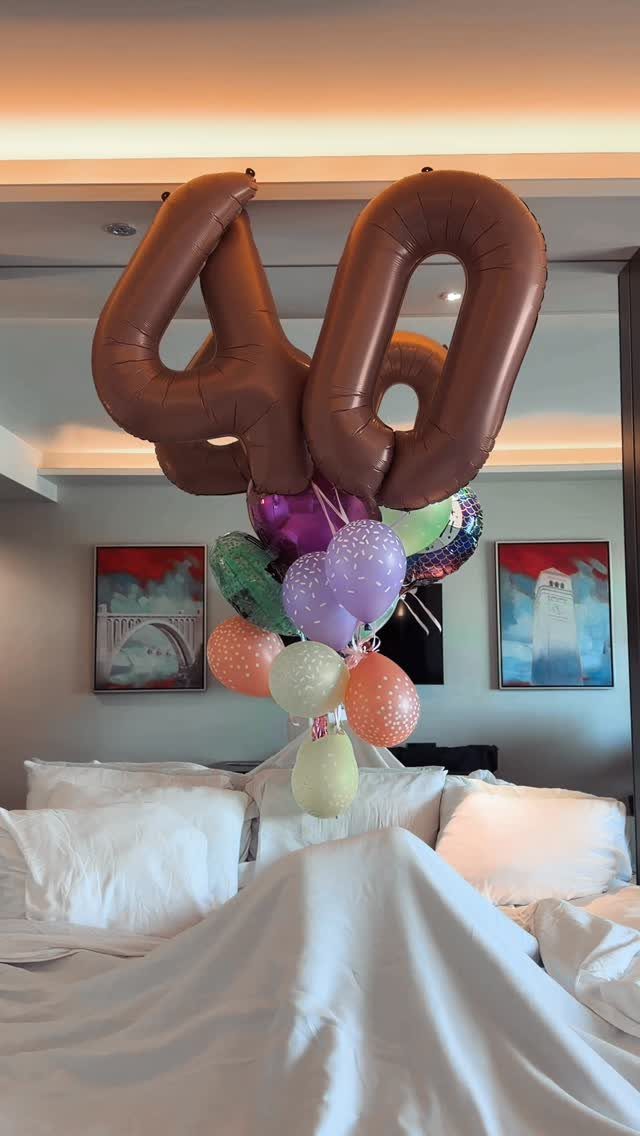 Bronze number 40 foil balloons floating above colorful balloons on a white bed.