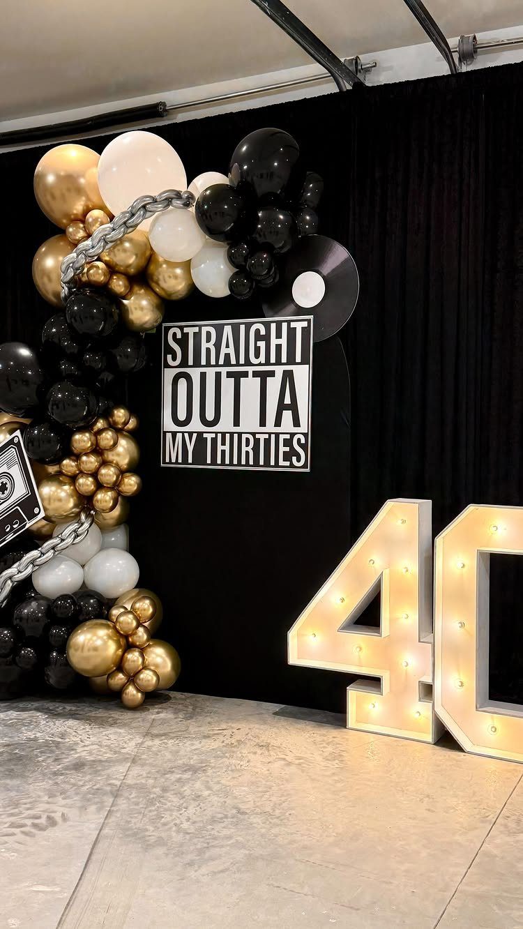 Birthday party decorations featuring a black and gold balloon arch and lit 40 numbers.